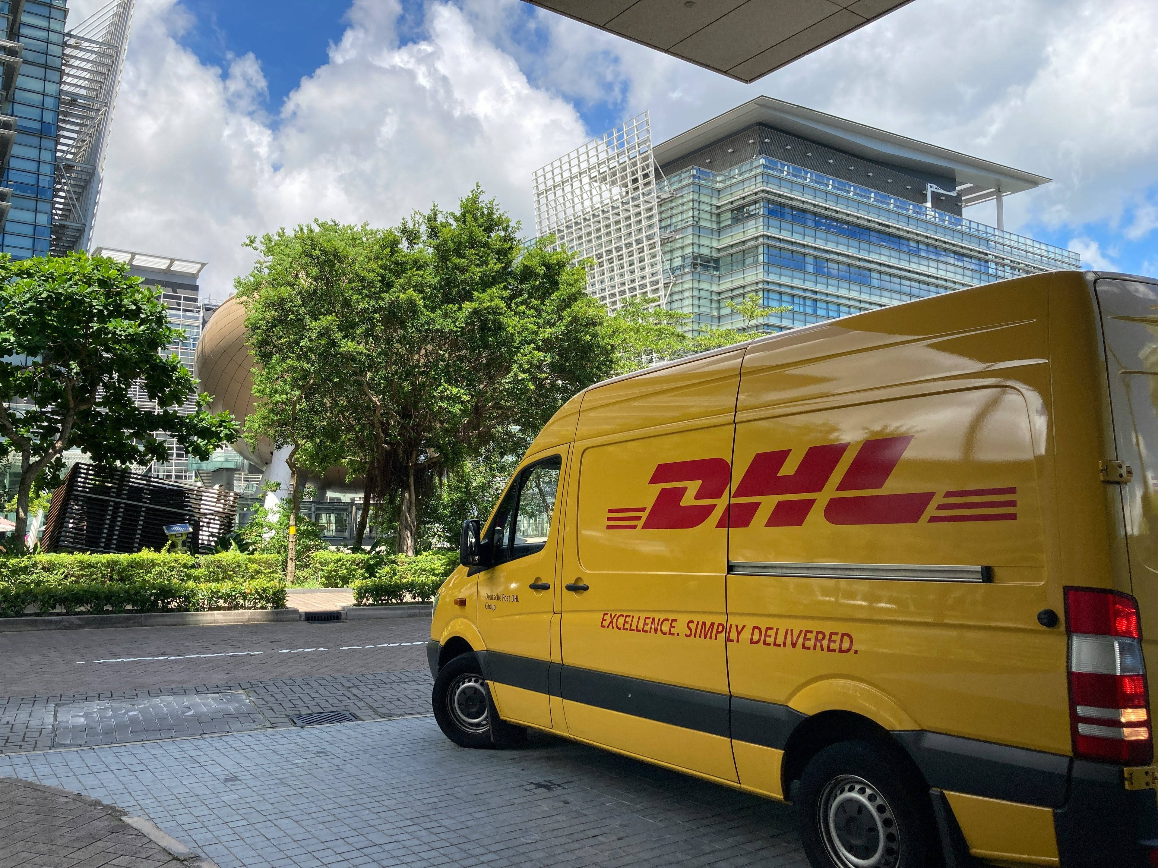 Yellow DHL delivery van parked on a city street with modern buildings in the background.