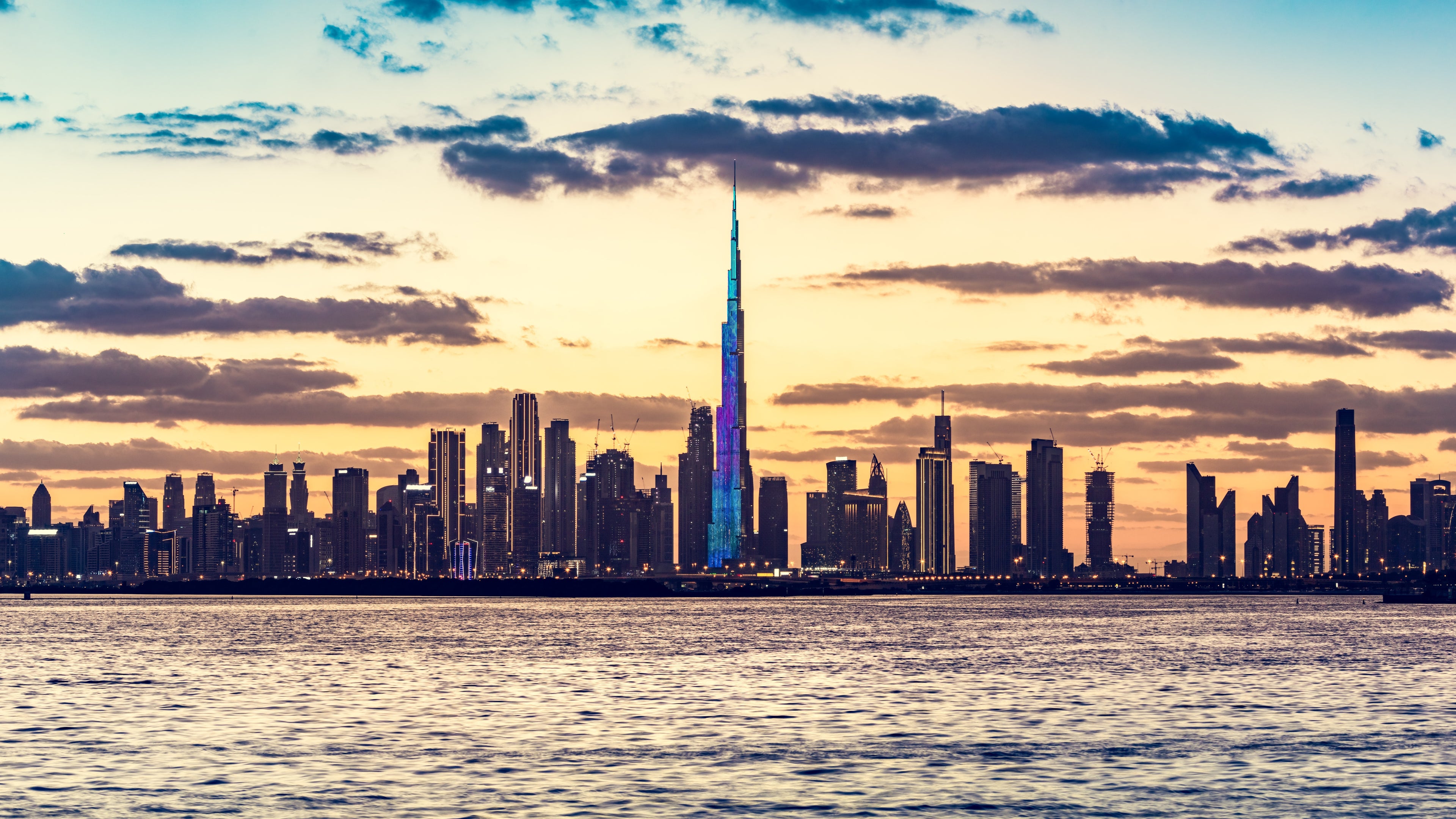 City skyline with a prominent tower at sunset, viewed from across water.